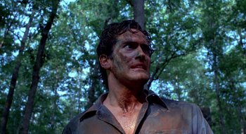 Movie still from “Evil Dead II” (1987), directed by Sam Raimi – A person wearing a dirty shirt near a tree; Close Up shot, Low angle