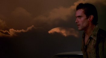 Movie still from “Evil Dead II” (1987), directed by Sam Raimi – A man standing in front of a cloud filled sky; Close Up shot, Low angle
