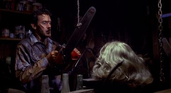 Movie still from “Evil Dead II” (1987), directed by Sam Raimi – A man holding a chainsaw in front of a woman with blonde hair; Medium shot, Over the shoulder angle