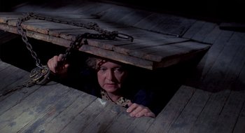 Movie still from “Evil Dead II” (1987), directed by Sam Raimi – A woman is hiding under a wooden box; Medium shot, High angle