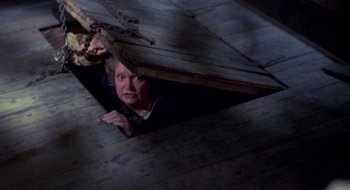 Movie still from “Evil Dead II” (1987), directed by Sam Raimi – A woman hiding under a wooden floor in the dark; Wide shot, Overhead angle