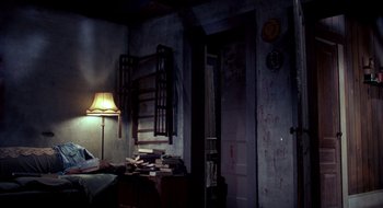 Movie still from “Evil Dead II” (1987), directed by Sam Raimi – A room with a bed , a lamp , and a clock on the wall; Wide shot, High angle