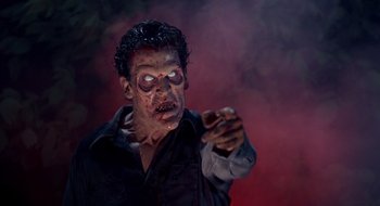 Movie still from “Evil Dead II” (1987), directed by Sam Raimi – A man with a zombie face pointing at the camera; Medium shot, Low angle