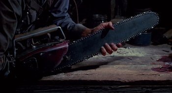Movie still from “Evil Dead II” (1987), directed by Sam Raimi – A man holding a chain saw in a workshop; Extreme Close Up shot, Low angle