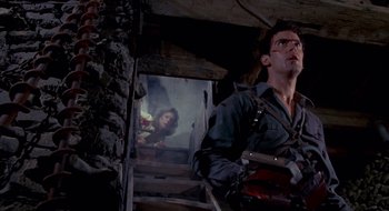Movie still from “Evil Dead II” (1987), directed by Sam Raimi – A man standing next to stairs with a painting on the wall; Medium shot, Low angle