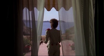 Movie still from “Evil Under the Sun” (1982), directed by Guy Hamilton – A woman standing in front of a window looking out at the ocean; Wide shot, Over the shoulder angle