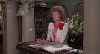 Movie still from “Evil Under the Sun” (1982), directed by Guy Hamilton – An older woman sitting at a desk in front of a book; Medium shot, Over the shoulder angle