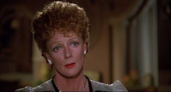 Movie still from “Evil Under the Sun” (1982), directed by Guy Hamilton – An older woman wearing a necklace and earrings; Close Up shot, Over the shoulder angle