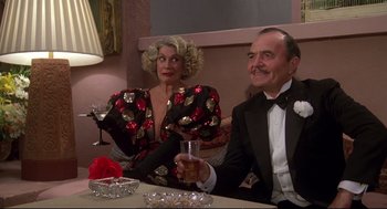 Movie still from “Evil Under the Sun” (1982), directed by Guy Hamilton – A man and a woman sitting at a table with a drink; Medium shot, Low angle