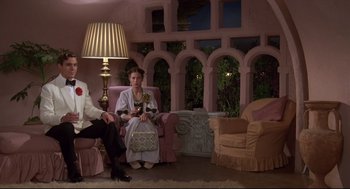 Movie still from “Evil Under the Sun” (1982), directed by Guy Hamilton – A man and a woman sitting on a pink couch; Wide shot, Low angle