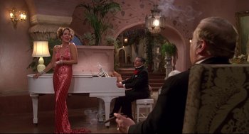 Movie still from “Evil Under the Sun” (1982), directed by Guy Hamilton – A woman in a red dress standing in front of a white piano; Wide shot, Low angle