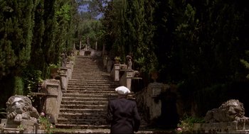 Movie still from “Evil Under the Sun” (1982), directed by Guy Hamilton – An old man wearing a hat sitting in front of a set of stairs; Wide shot, Low angle