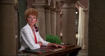 Movie still from “Evil Under the Sun” (1982), directed by Guy Hamilton – An older woman sitting at a table with a book; Medium shot, Over the shoulder angle