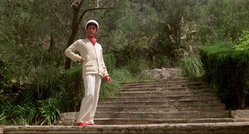 Movie still from “Evil Under the Sun” (1982), directed by Guy Hamilton – A man standing on some steps wearing a white hat; Wide shot, Low angle