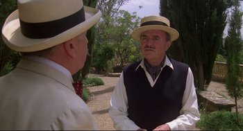 A man in a straw hat talking to another man in a vest
