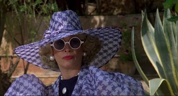 Movie still from “Evil Under the Sun” (1982), directed by Guy Hamilton – A woman wearing a hat and sunglasses in a garden setting; Close Up shot, Low angle