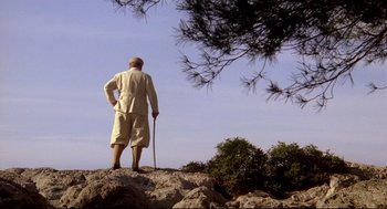Movie still from “Evil Under the Sun” (1982), directed by Guy Hamilton – A man standing on top of a hill with a cane; Wide shot, Low angle