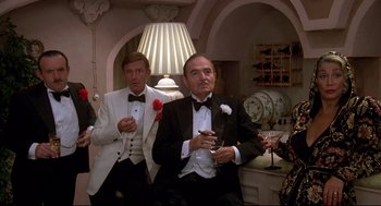 Movie still from “Evil Under the Sun” (1982), directed by Guy Hamilton – Two men in tuxedos sitting next to each other holding drinks; Medium shot, High angle
