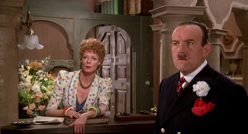 Movie still from “Evil Under the Sun” (1982), directed by Guy Hamilton – An older man and a younger woman sitting at a table; Medium shot, Low angle