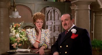 Movie still from “Evil Under the Sun” (1982), directed by Guy Hamilton – A man and a woman sitting at a table in a room; Medium shot, Low angle