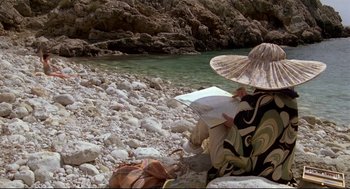Movie still from “Evil Under the Sun” (1982), directed by Guy Hamilton – A woman sitting on a rock near a river; Wide shot, High angle