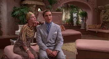 Movie still from “Evil Under the Sun” (1982), directed by Guy Hamilton – A man and a woman sitting on a couch in a room; Medium shot, Low angle