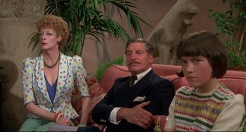 Movie still from “Evil Under the Sun” (1982), directed by Guy Hamilton – A man sitting on a couch next to two women; Medium shot, Over the shoulder angle