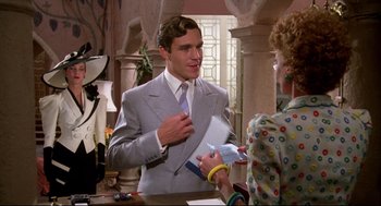 Movie still from “Evil Under the Sun” (1982), directed by Guy Hamilton – A man wearing a suit and tie talking to a woman; Medium shot, Over the shoulder angle