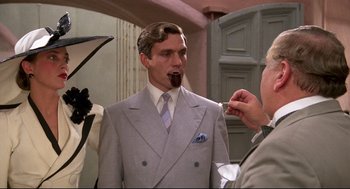 Movie still from “Evil Under the Sun” (1982), directed by Guy Hamilton – A man wearing a suit and tie eating a piece of chocolate; Medium shot, Over the shoulder angle