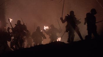 Movie still from “Excalibur” (1981), directed by John Boorman – A group of people are fighting with swords in the dark; Wide shot, Low angle