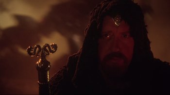 Movie still from “Excalibur” (1981), directed by John Boorman – A man with a beard is holding a golden key; Close Up shot, Low angle