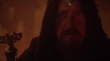 Movie still from “Excalibur” (1981), directed by John Boorman – A person with a beard wearing a hood; Close Up shot, Over the shoulder angle