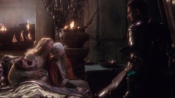 Movie still from “Excalibur” (1981), directed by John Boorman – Two people in medieval garb in a room with a fire; Wide shot, Over the shoulder angle