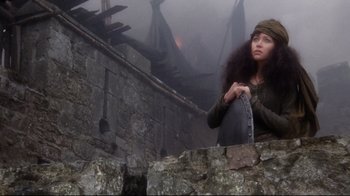 Movie still from “Excalibur” (1981), directed by John Boorman – A woman standing next to a stone wall in the fog; Medium shot, Low angle