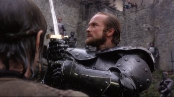 Movie still from “Excalibur” (1981), directed by John Boorman – A man dressed as a medieval knight holding a sword; Close Up shot, Over the shoulder angle