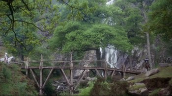 Movie still from “Excalibur” (1981), directed by John Boorman – A wooden bridge over a river in a forest; Extreme Wide shot, Low angle