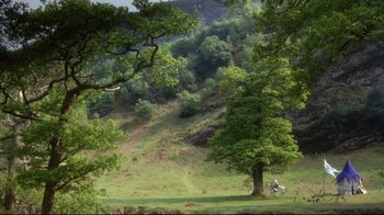 Movie still from “Excalibur” (1981), directed by John Boorman – Two people sitting on a bench under a large tree; Extreme Wide shot, High angle