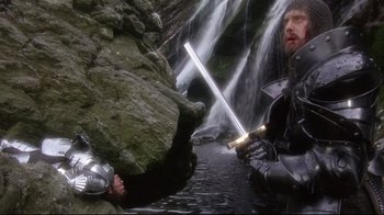 Movie still from “Excalibur” (1981), directed by John Boorman – Two men in armor are fighting in front of a waterfall; Wide shot, High angle