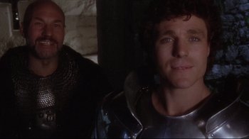 Movie still from “Excalibur” (1981), directed by John Boorman – A man wearing a suit of armor next to another man wearing armor; Close Up shot, Over the shoulder angle