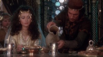 Movie still from “Excalibur” (1981), directed by John Boorman – A man and a woman sitting at a table; Medium shot, Over the shoulder angle