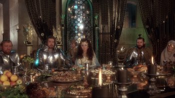 Movie still from “Excalibur” (1981), directed by John Boorman – A group of people sitting at a table with plates of food on top of it; Wide shot, High angle