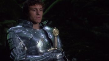 Movie still from “Excalibur” (1981), directed by John Boorman – A man in a suit of armor holding a sword; Medium shot, Low angle