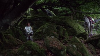 Movie still from “Excalibur” (1981), directed by John Boorman – A man sitting on the rocks in the woods; Wide shot, High angle