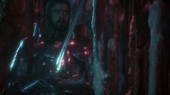 Movie still from “Excalibur” (1981), directed by John Boorman – A man with a beard and a helmet on holding a sword in his hand; Medium shot, Over the shoulder angle