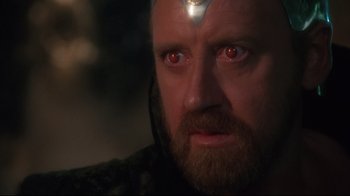 Movie still from “Excalibur” (1981), directed by John Boorman – A person with a beard and red eyes; Close Up shot, Over the shoulder angle
