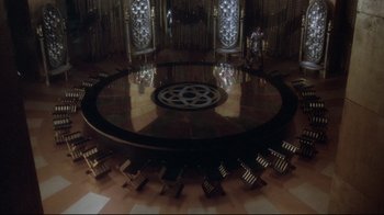 Movie still from “Excalibur” (1981), directed by John Boorman – A large round table with chairs around it in a room; Extreme Wide shot, High angle
