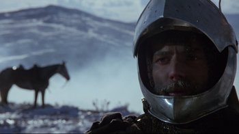 Movie still from “Excalibur” (1981), directed by John Boorman – A person wearing a helmet with a horse in the background; Close Up shot, Low angle