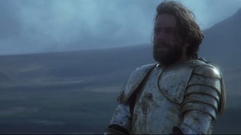Movie still from “Excalibur” (1981), directed by John Boorman – A man with a beard wearing a suit of armor; Medium shot, Low angle