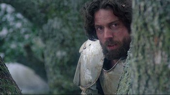 Movie still from “Excalibur” (1981), directed by John Boorman – A man with a beard wearing a white armor; Medium shot, Low angle