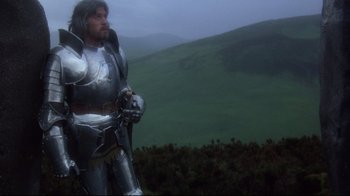 Movie still from “Excalibur” (1981), directed by John Boorman – A man dressed as a knight standing in front of a hill; Medium shot, Low angle